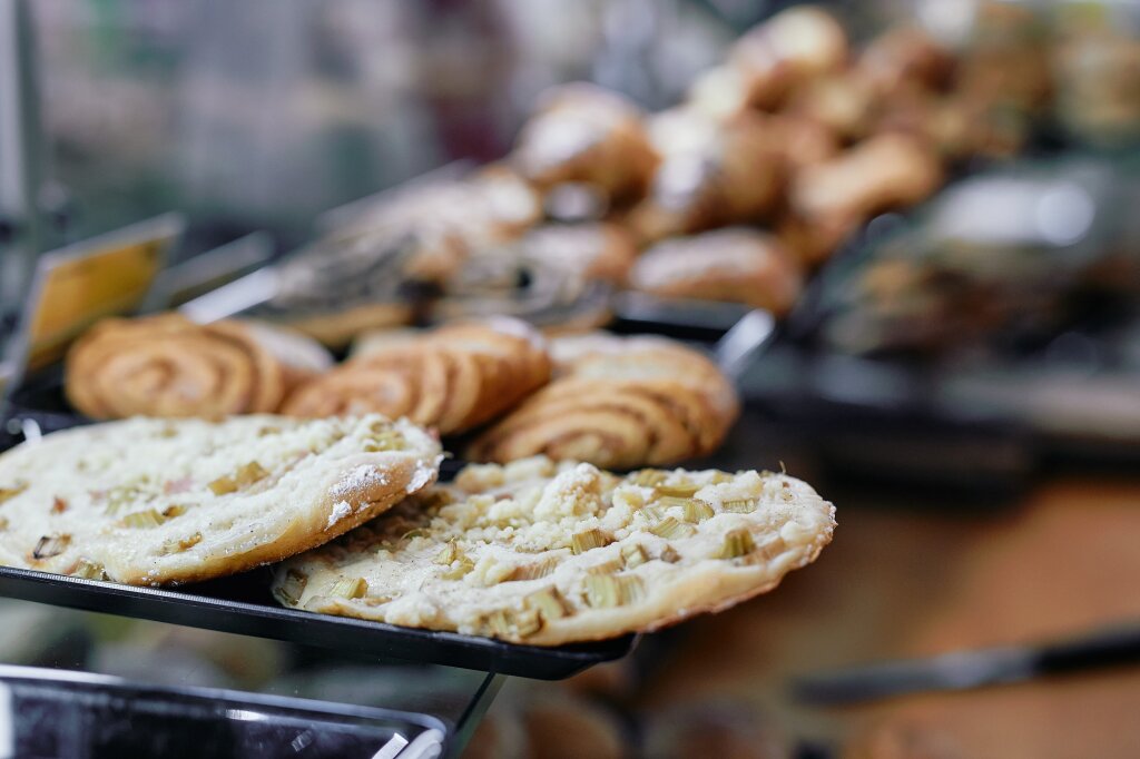 Verschiedene Backwaren, darunter runde Stücke mit Rhabarberstreuseln und Schnecken, liegen in einer Auslage einer Bäckerei.